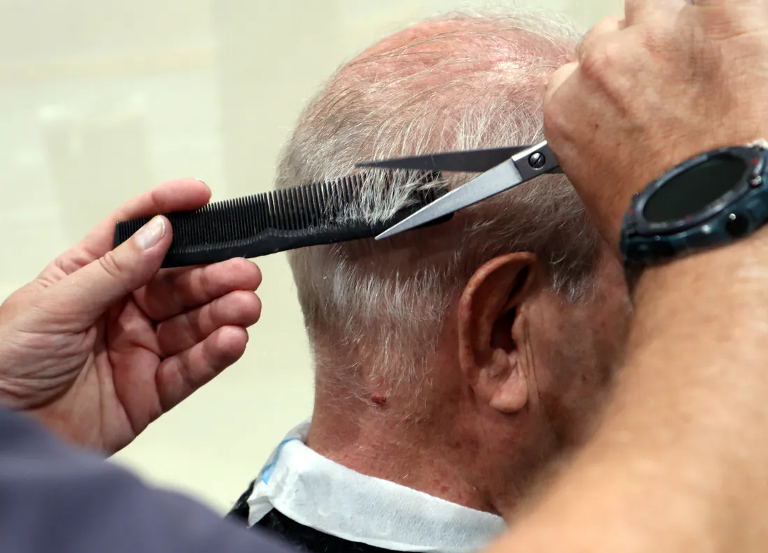 Manos del barbero rematando la nuca de un cliente con tijera y peine.